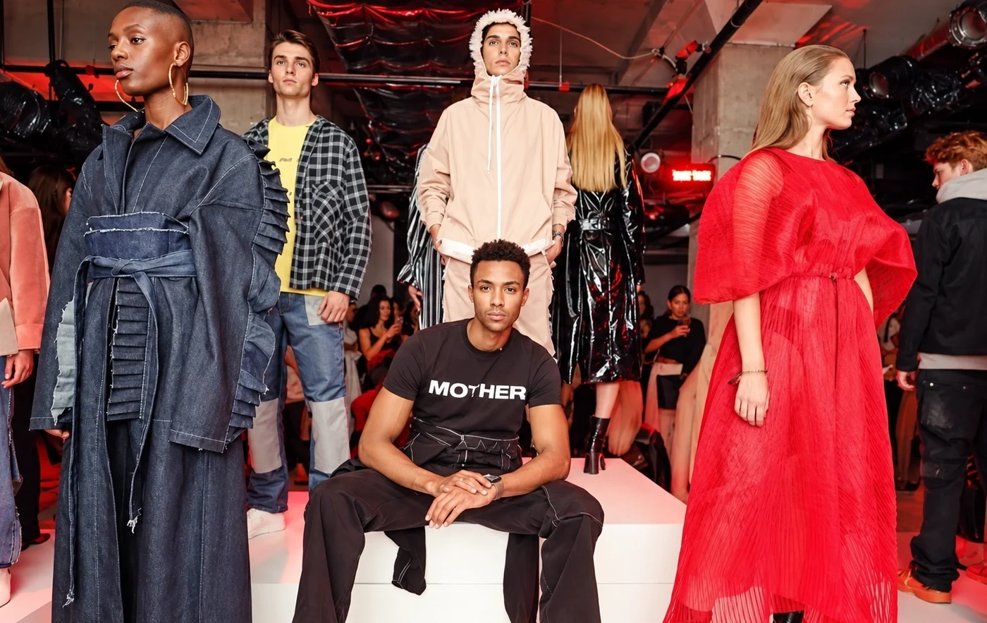 Group runway fashion photograph featuring contemporary collections under red stage lighting.